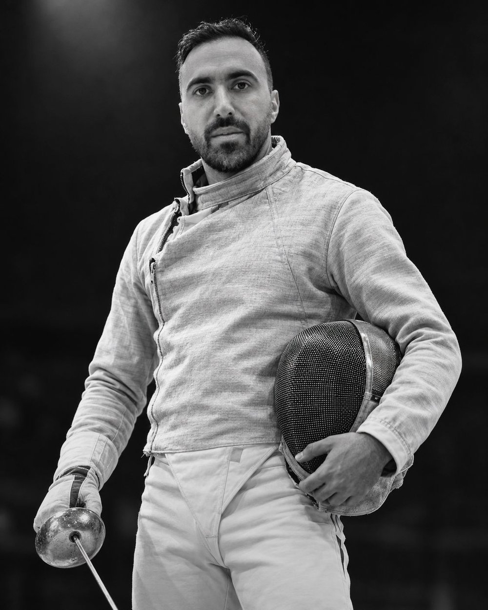 Black and white portrait of fencer Ali Pakdaman holding his mask and sabre