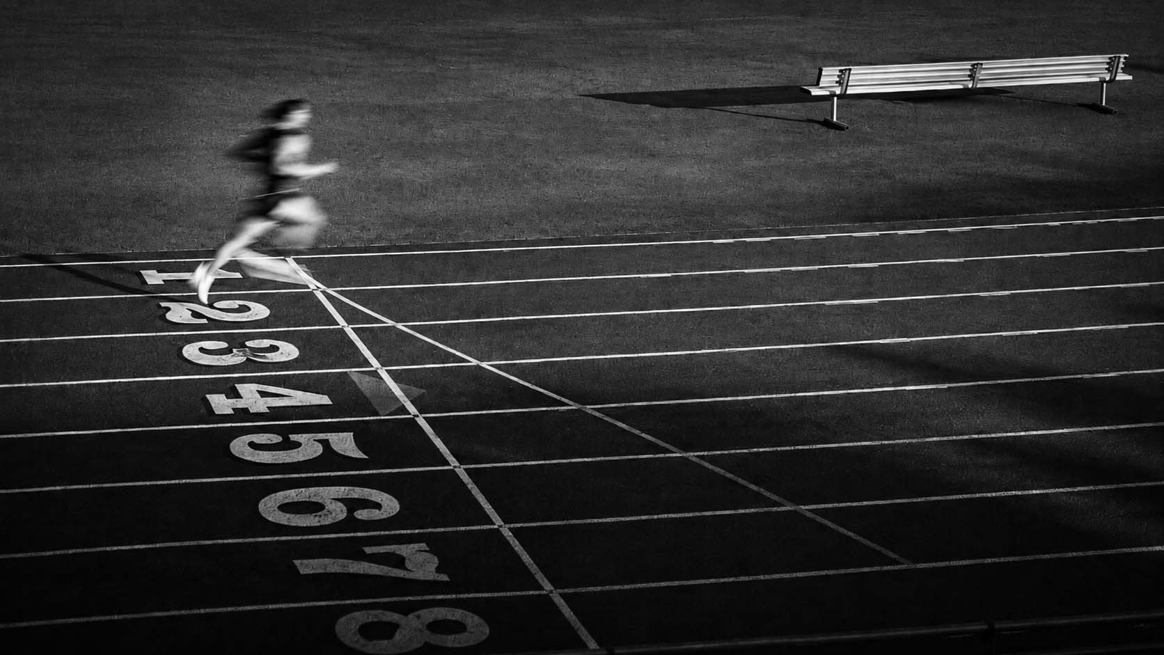 A sprinter blurs across the start line of an empty track